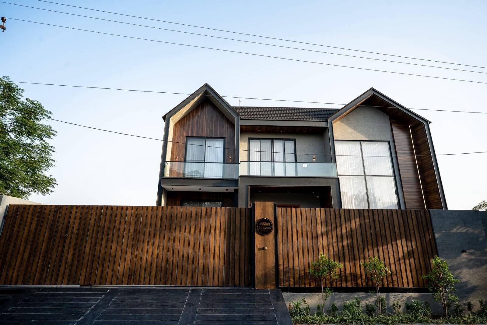 Una casa moderna de dos pisos con fachada de madera, ventanas grandes y entrada protegida por una reja.