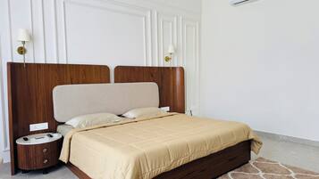 A bedroom with a wooden headboard, a beige bedspread, a round bedside table, and a wall-mounted air conditioner.