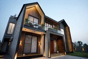 A modern two-story house with a balcony, large windows, and a well-lit entrance.