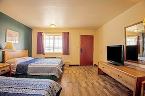 A hotel room with two beds, a TV, a dresser, a window with curtains, and a door.