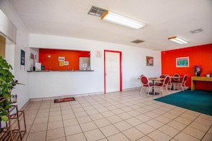 Un hall d’hôtel comprenant un comptoir d’accueil, une porte, un espace repas avec des chaises et une moquette verte.