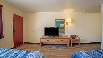 Habitación de hotel con dos camas, un televisor sobre un soporte de madera, una silla y una lámpara fijada a la pared.