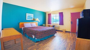 A bedroom with a bed, bedside table, lamp, window with curtains, and a television.