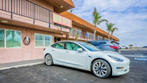 A white Tesla parked in front of a building with a 'NOW OPEN' sign.