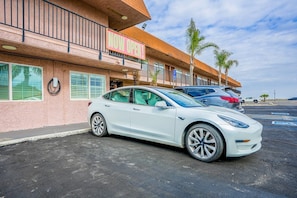 Un Tesla blanco estacionado frente a un edificio con un letrero que dice 'NOW OPEN'.