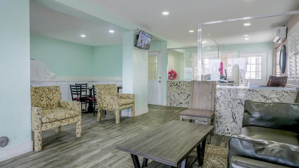 A room with a wooden floor, a dining table, two patterned chairs, a sofa, and a TV mounted on the wall. - King Bed Non-Smoking (Buttonwillow, CA)