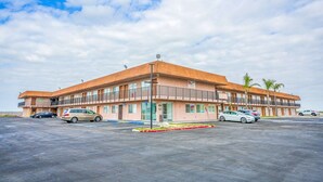A multi-story motel with a flat roof, multiple balconies, and a parking lot.