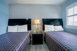 Una habitación de hotel con dos camas, una mesita de noche con lámpara y una ventana con persianas.