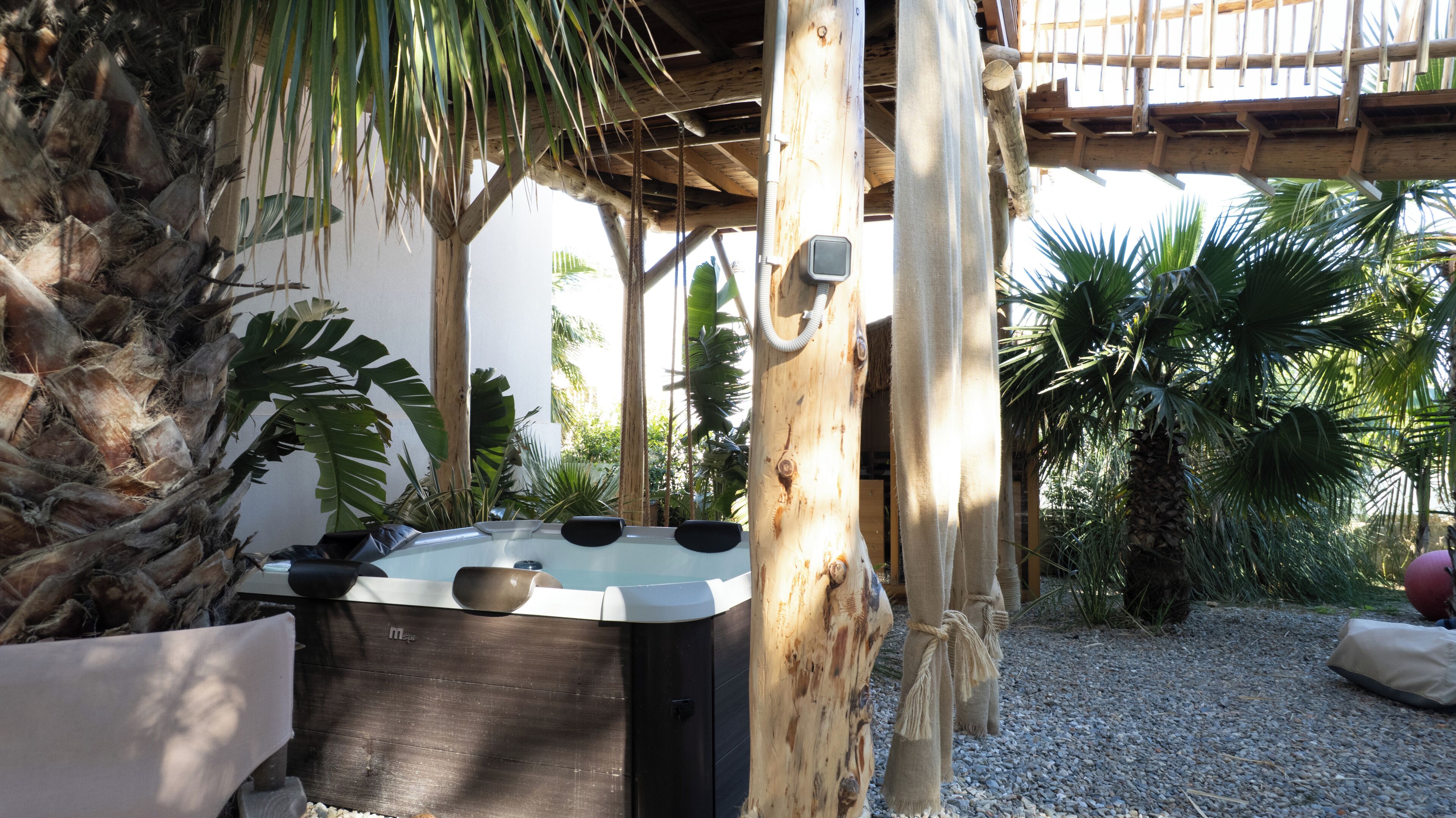 Zona de spa con jacuzzi, pérgola de madera y plantas tropicales.