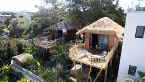 Una casa en el árbol con techo de paja, terraza de madera y zona de estar al aire libre.
