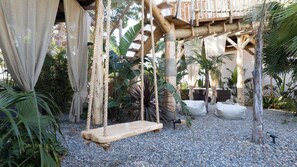 A wooden swing set, a rope ladder, and a covered seating area in a garden with gravel ground.
