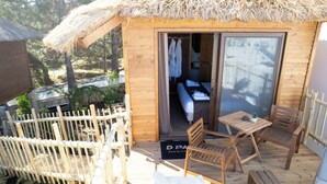 Una cabana de fusta amb teulada de palla, un balcó amb mobles de fusta i un llit visible a l'interior.