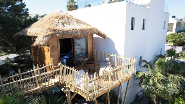 A wooden cabin with a thatched roof, a balcony with a wooden railing, and a view of the surrounding area.