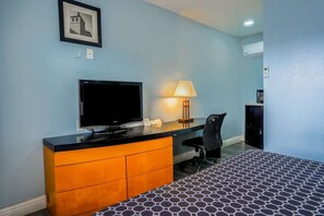 Una habitación de hotel con una cama, un escritorio con televisor, una lámpara y una silla.