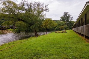 Blick auf einen Fluss mit Picknicktisch, Holzzaun und einem Gebäude mit überdachtem Gang.