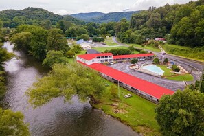 Un edificio con techo rojo, junto a un río, rodeado de vegetación y colinas.