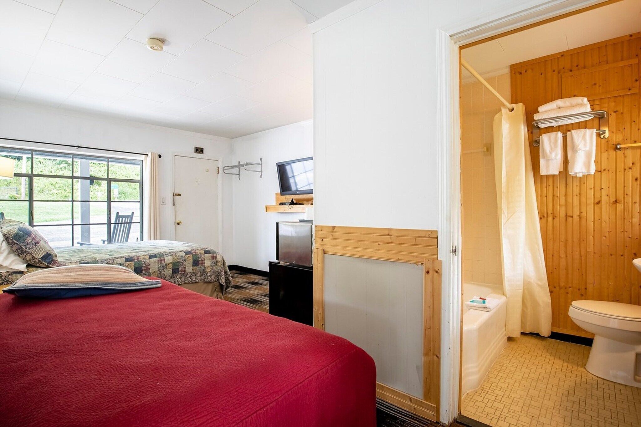 A bedroom with a bed, a television, a small desk, and a bathroom with a shower and toilet.