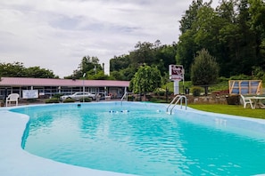Ein Schwimmbecken mit Rettungsschwimmer-Schild, überdachtem Bereich und einem Gebäude im Hintergrund.