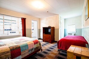 Quarto de hotel com duas camas, uma cômoda de madeira, uma televisão e uma janela com cortinas.