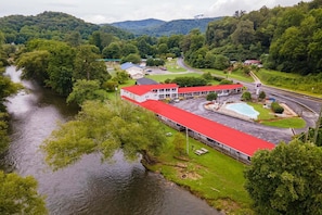 Um edifício com telhado vermelho, ao lado de um rio, rodeado por vegetação e colinas.