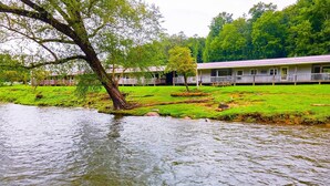 A riverside hotel with a grassy lawn, a tree, and a building with a porch.