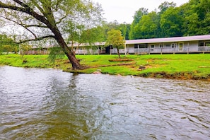 A riverside hotel with a grassy lawn, a tree, and a building with a porch.