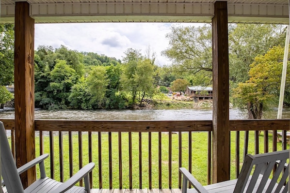 A wooden deck with chairs overlooking a river and greenery.
