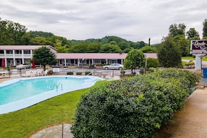 Uma área de piscina com um edifício ao fundo, uma placa com o nome Lloyds Country Inn e vista para o verde ao redor.