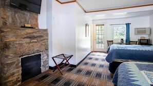 A room with a stone fireplace, a bed with a blue quilt, a television, and a door leading to a balcony.
