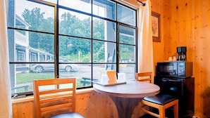 Una habitación con un ventanal grande, paredes de madera, una mesa redonda, dos sillas y un televisor negro pequeño.