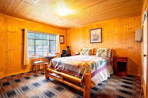 Um quarto com painéis de madeira, uma cama, uma cadeira, uma mesinha, uma janela e uma porta.