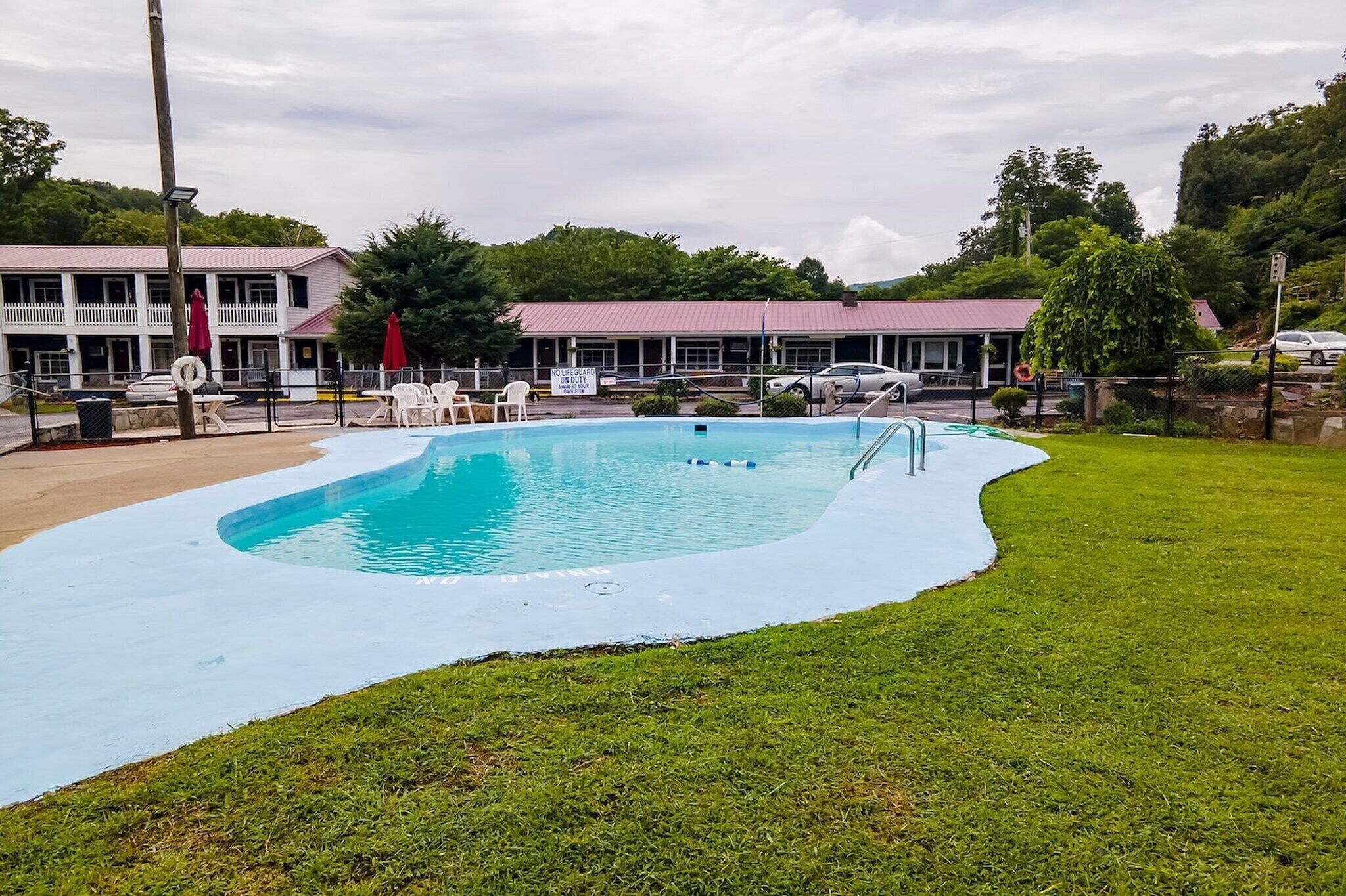 A swimming pool with a curved edge, surrounded by a grassy area and a building with a red roof in the background.