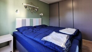 Quarto com cama, luminárias de cabeceira, guarda-roupa e um objeto decorativo na parede.