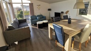 Uma sala de estar moderna com sofá, duas poltronas, uma mesa de jantar com cadeiras, televisão e abajur.
