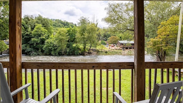 Een houten terras met stoelen met uitzicht op een rivier en groen.