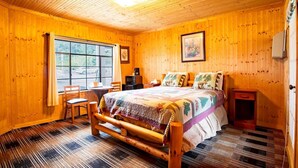 Een kamer met houten lambrisering, een bed, een stoel, een tafeltje en een raam.