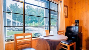 Een kamer met een groot raam, houten wanden, een ronde tafel, twee stoelen en een kleine, zwarte televisie.