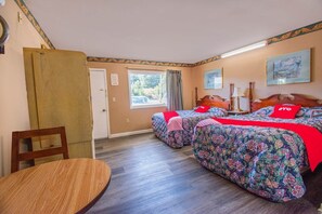 Una habitación con dos camas, una mesa de madera, un ventanal con cortinas y una puerta.