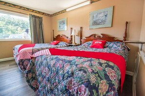A bedroom with a large bed, two bedside tables, a window with curtains, and two framed pictures on the wall.