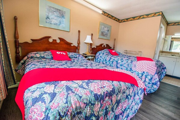 Une chambre d’hôtel avec deux lits, chacun agrémenté de draps à motifs floraux et de touches de couleur rouge, une table de chevet avec une lampe et des œuvres d’art accrochées aux murs.