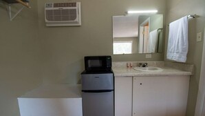 Un baño pequeño con un lavamanos blanco, un espejo, una toalla colgada en la pared y un refrigerador compacto.