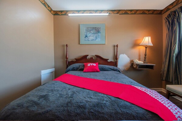 A hotel room with a bed, a bedside lamp, a framed picture on the wall, and a red throw blanket.