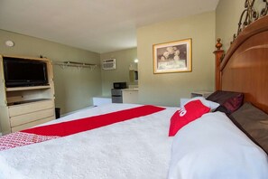 Une chambre d’hôtel équipée d’un lit, d’une télévision, d’un four à micro-ondes, d’un petit bureau et d’un tableau encadré au mur.
