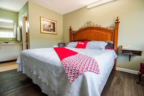A hotel room with a bed, a bedside table, a mirror, and a small shelf.