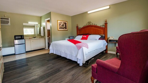 Ein Hotelzimmer mit einem Bett, einem roten Sessel, einer Küchenzeile und einem Bild an der Wand.