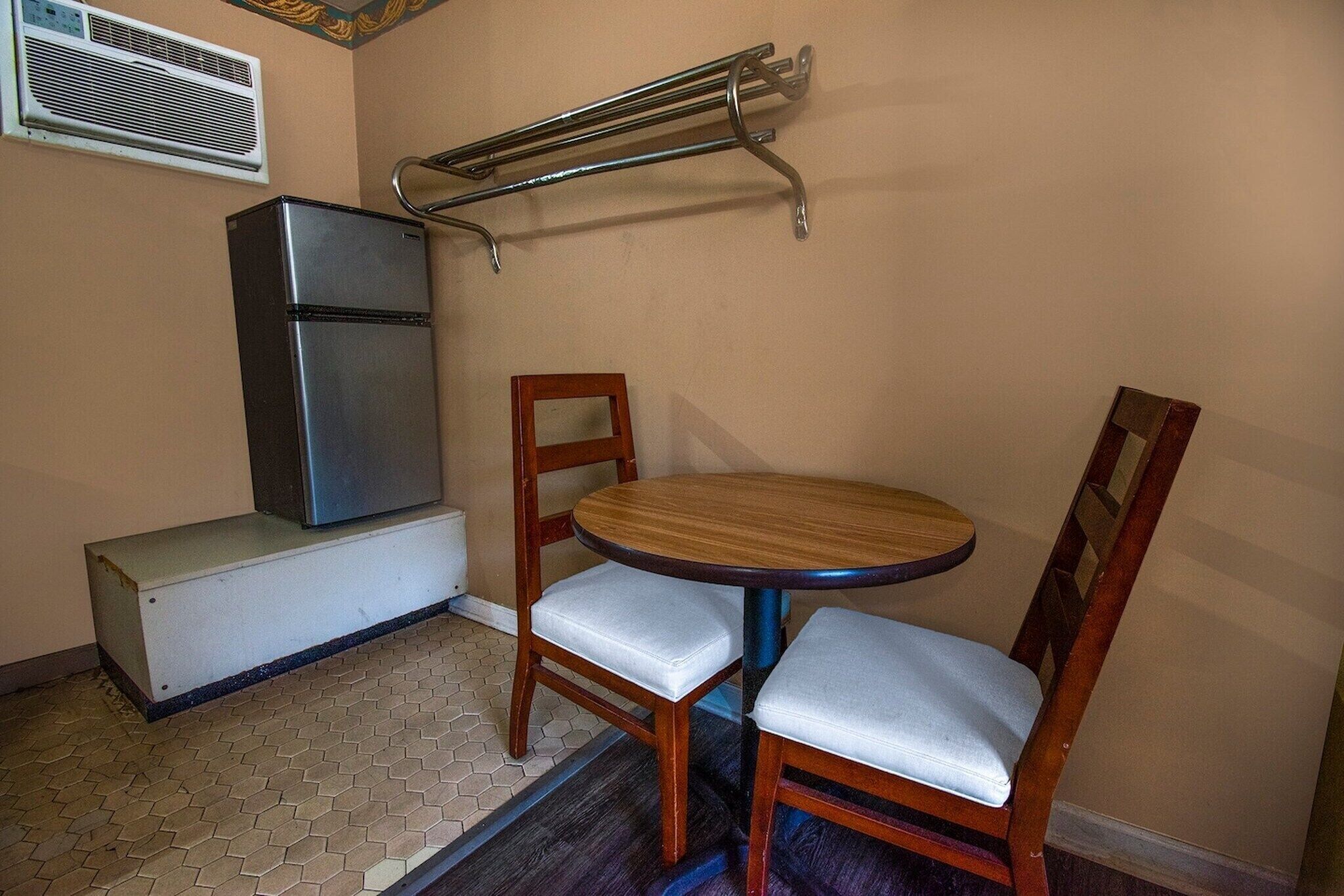 A compact kitchen with a refrigerator, a small dining table, two chairs, and a metal rack on the wall.