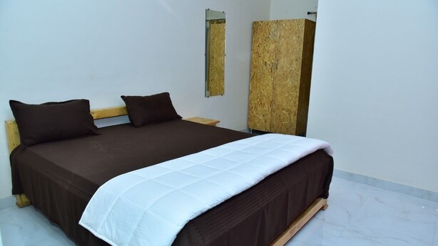 A bed with a brown bedspread and white quilt, a wooden headboard, a nightstand with a mirror, and a large wooden cabinet.