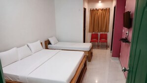 A room with two wooden beds, a pair of red chairs, a television mounted on the wall, and a green door.