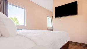 Una camera d'albergo con un letto, una televisione a muro e una finestra con tende.