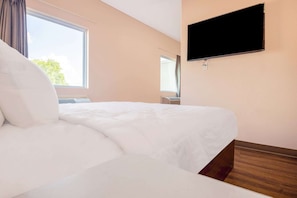 A hotel room with a bed, a television mounted on the wall, and a window with curtains.